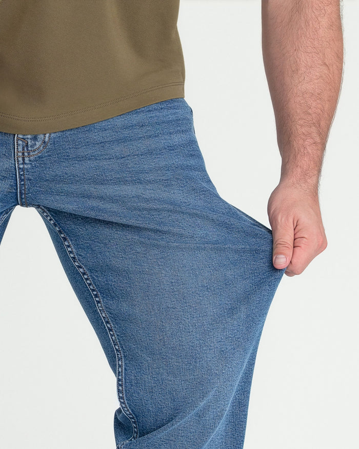 Man wearing medium blue athletic fit jeans with tan t-shirt, side view showing fit through thigh and leg.