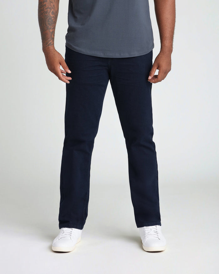 Man wearing deep blue t-shirt and dark navy athletic fit jeans with white sneakers.
