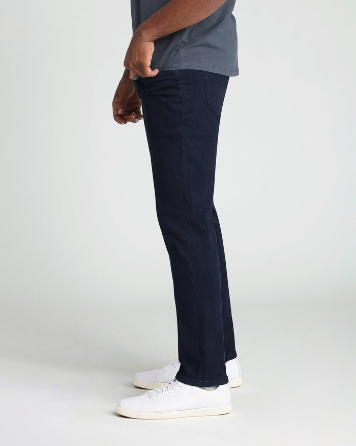Man wearing deep blue athletic fit jeans with a gray-blue shirt and white sneakers.