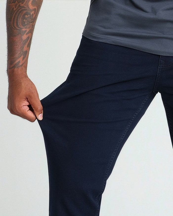 Deep blue athletic fit pants shown from waist down on a model wearing a gray-blue shirt, demonstrating the tapered leg fit.