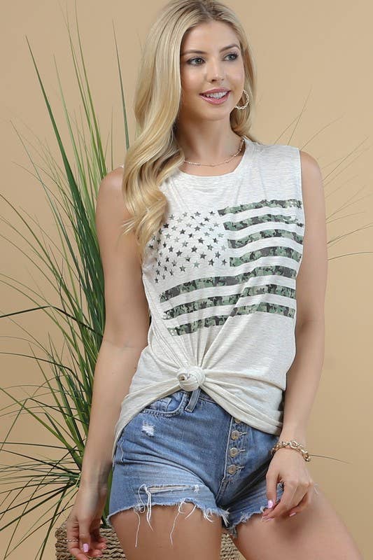 Woman wearing a white sleeveless top with black patterns and denim shorts against a beige background.