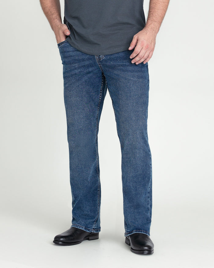 Man wearing medium blue bootcut jeans with a dark gray t-shirt and black shoes.