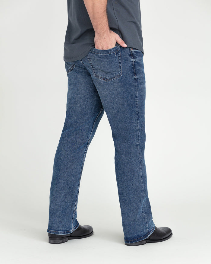 Medium blue bootcut jeans with five-pocket styling shown from side view on model wearing black boots.
