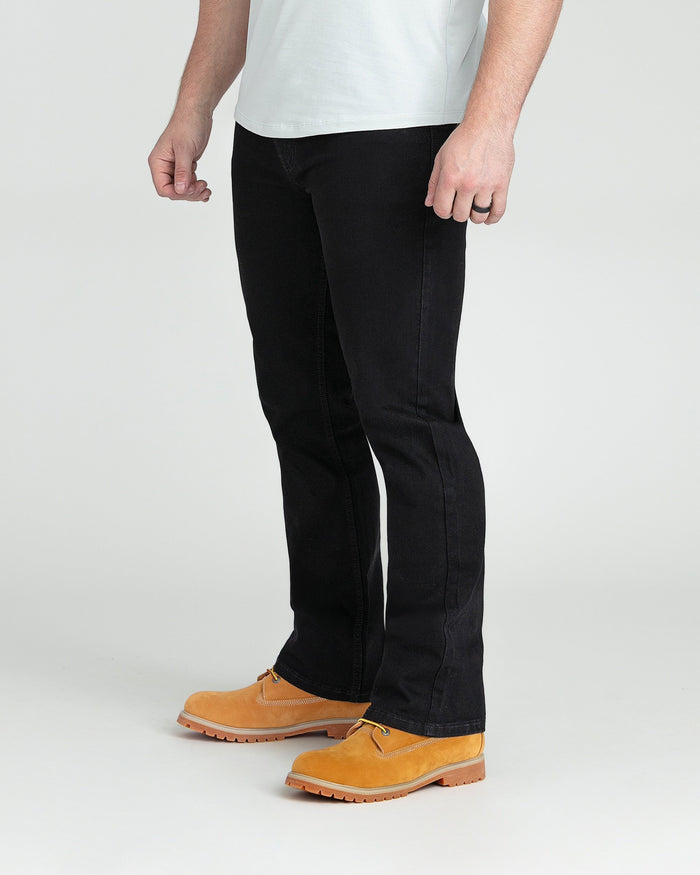 Black bootcut jeans with flared hem on model wearing white t-shirt and tan work boots.