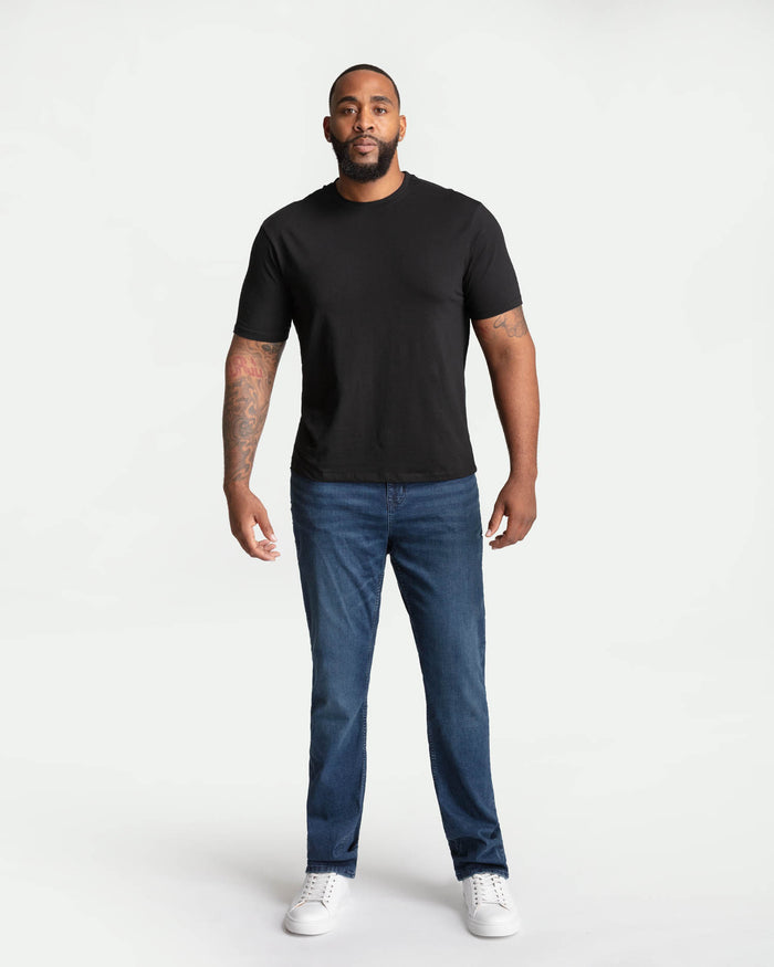 Man wearing black crew neck t-shirt and midnight blue bootcut jeans with white sneakers.