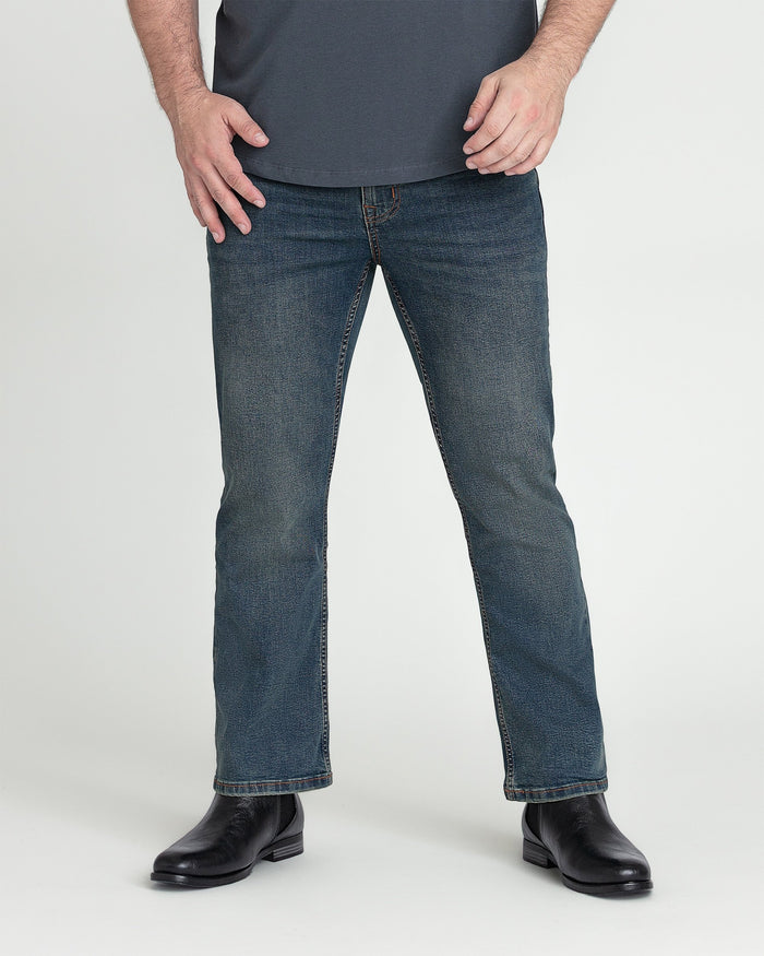 Man wearing tinted dark blue bootcut jeans with black boots and dark gray shirt.