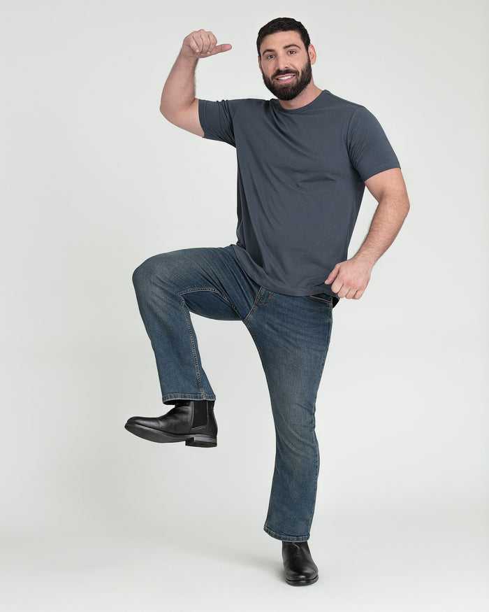 Man wearing tinted bootcut jeans with flared legs and a gray t-shirt, black boots visible.