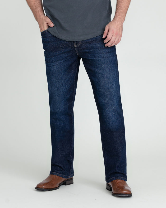 Dark blue bootcut jeans on a man wearing a gray shirt and brown cowboy boots.