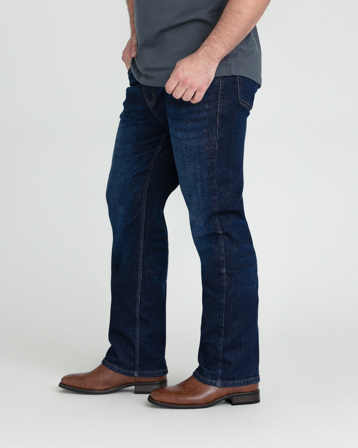 Dark blue bootcut jeans with flared hem, shown on male model wearing gray shirt and brown leather boots.