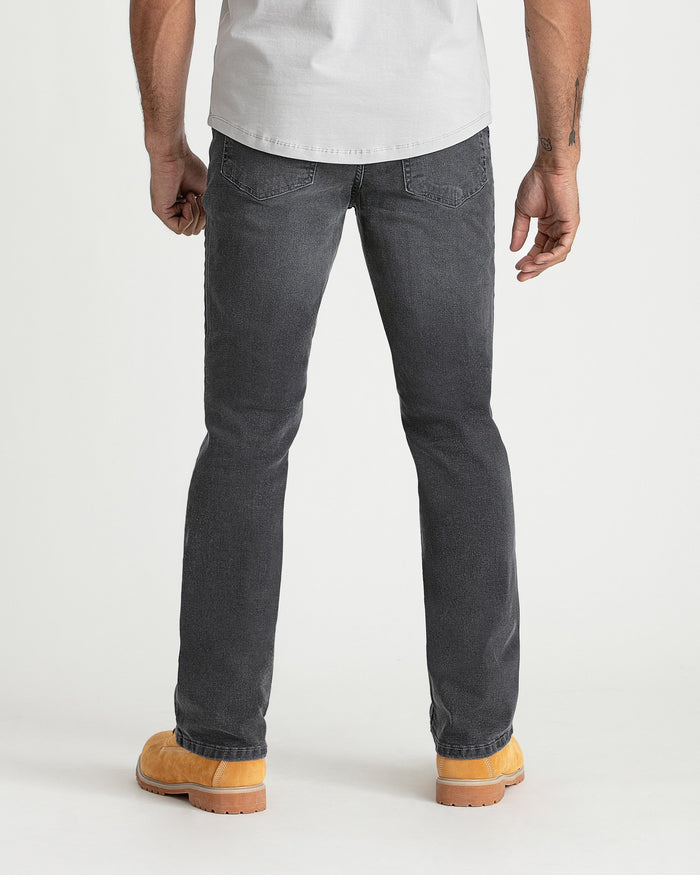 Man wearing grey bootcut jeans with white t-shirt and tan work boots, shown from back.