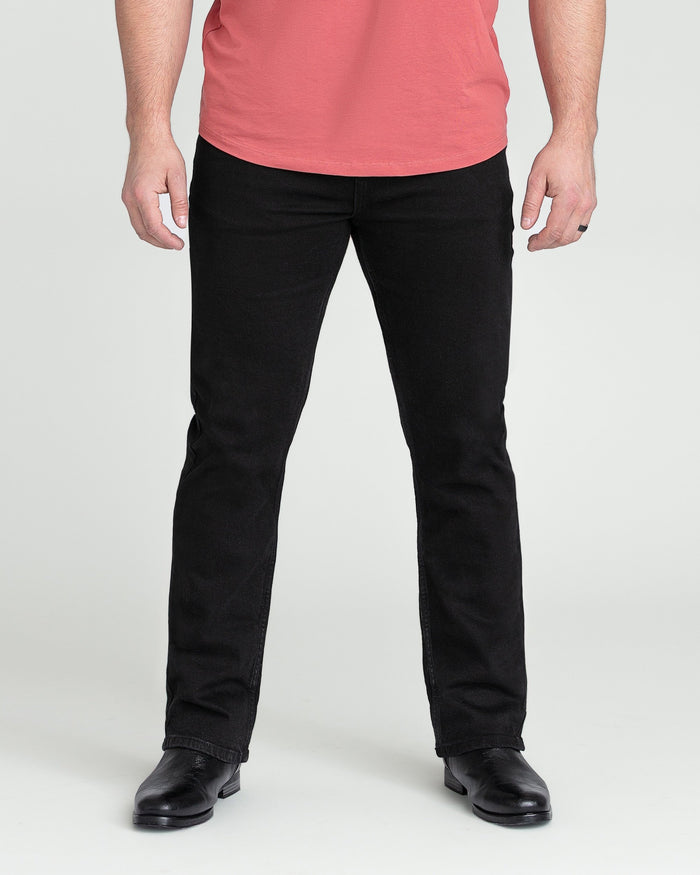 Black bootcut jeans on model wearing pink shirt and black shoes.