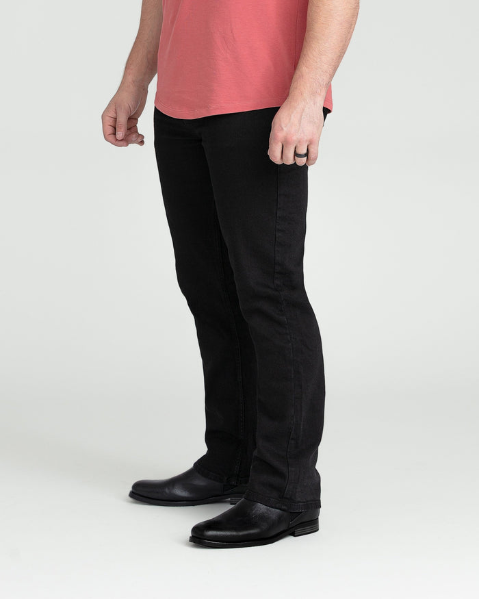 Black bootcut jeans on model wearing coral pink t-shirt and black leather shoes.