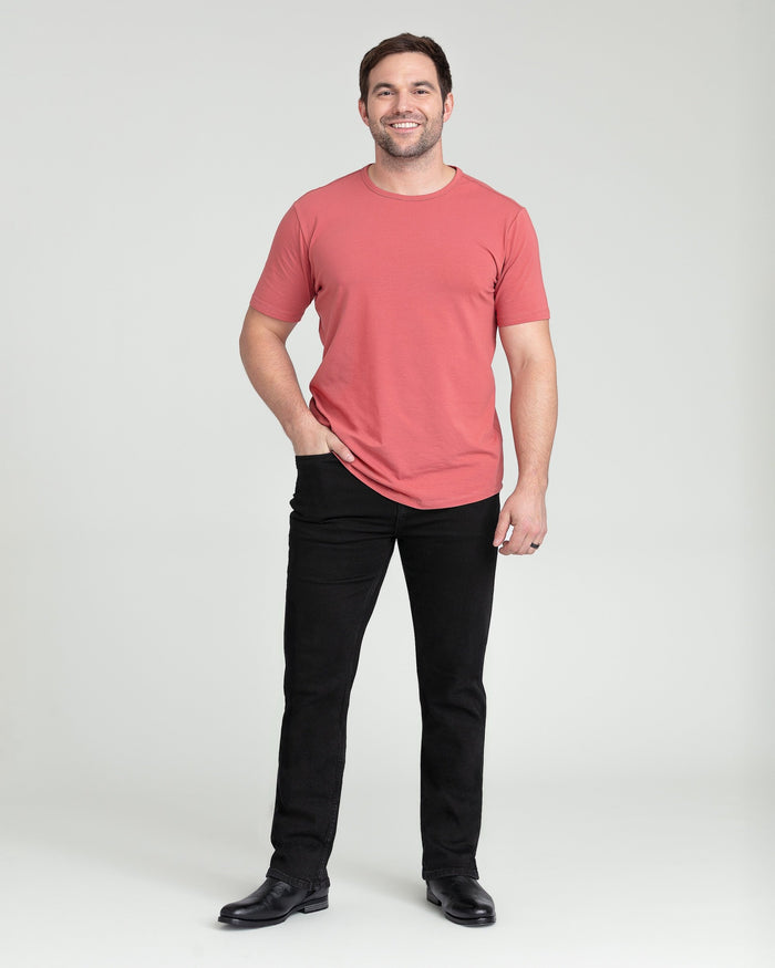 Man wearing coral short-sleeve t-shirt and black bootcut jeans with black shoes.
