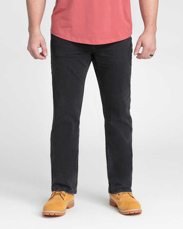 Faded black bootcut jeans on model wearing coral t-shirt and tan work boots.