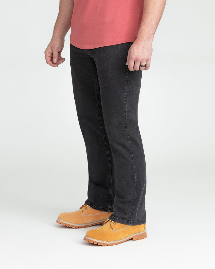 Man wearing faded black bootcut jeans with tan work boots and coral t-shirt.