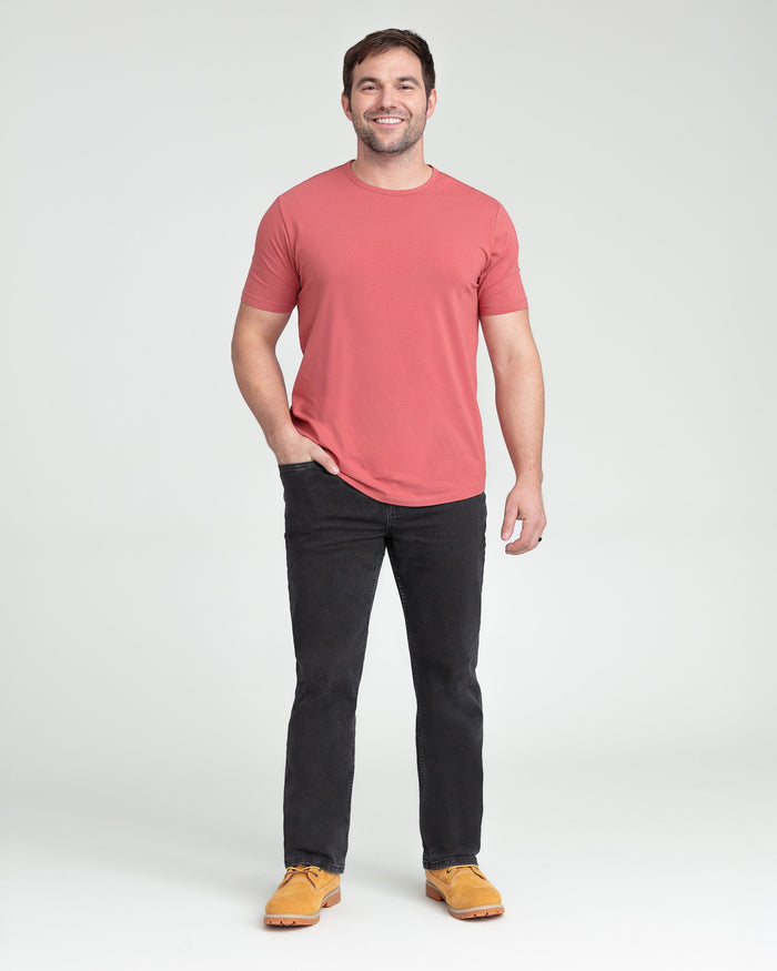 Man wearing coral short-sleeve t-shirt and faded black bootcut jeans with tan work boots.
