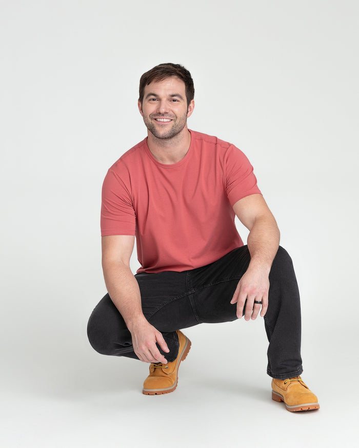 Man wearing faded black bootcut jeans with red t-shirt and tan work boots.