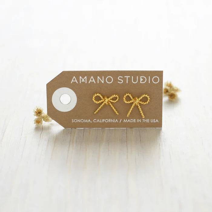 The earrings shown on a brown card with the text "Amano Studio; Sonoma, California, Made in the USA" printed on the card and dried flowers in the background.