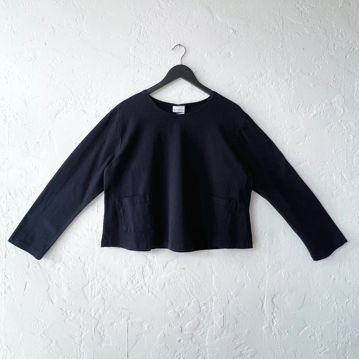Black long-sleeve top on a hanger against a white wall