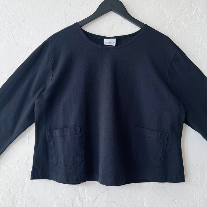Black long-sleeve shirt on a hanger against a white wall