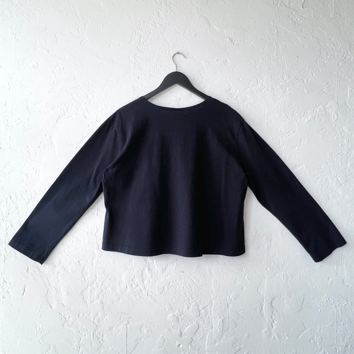 Black long-sleeve top on a hanger against a white wall, viewed from the back