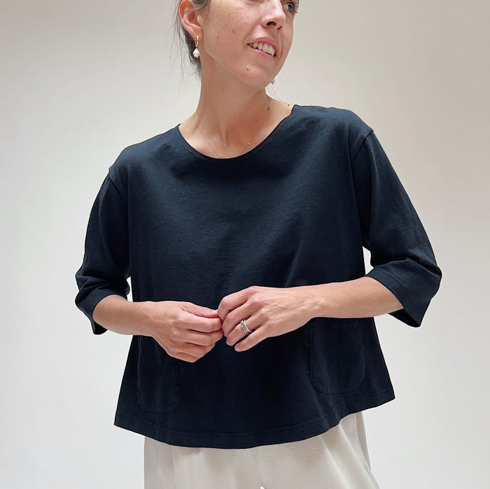 A person wearing a black, 3/4 sleeve top with two front pockets, made of cotton, in a casual setting