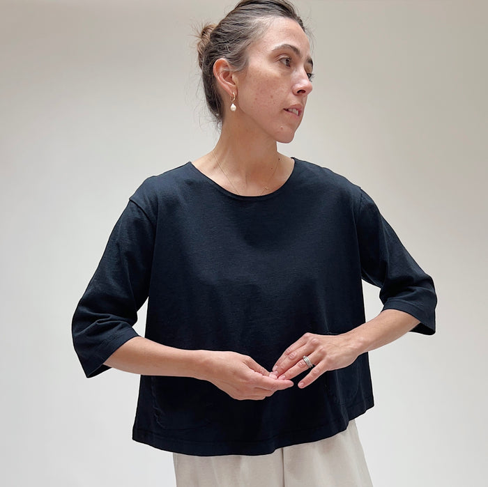 A person wearing a black, 3/4 sleeve top with two front pockets, made of cotton, in a casual setting