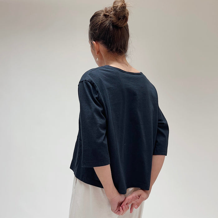 A person wearing a black, 3/4 sleeve top with two front pockets, viewed from the back