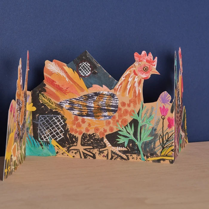 Three panels of a card with a rooster with a floral background shown unfolded  on a wooden surface against a navy wall