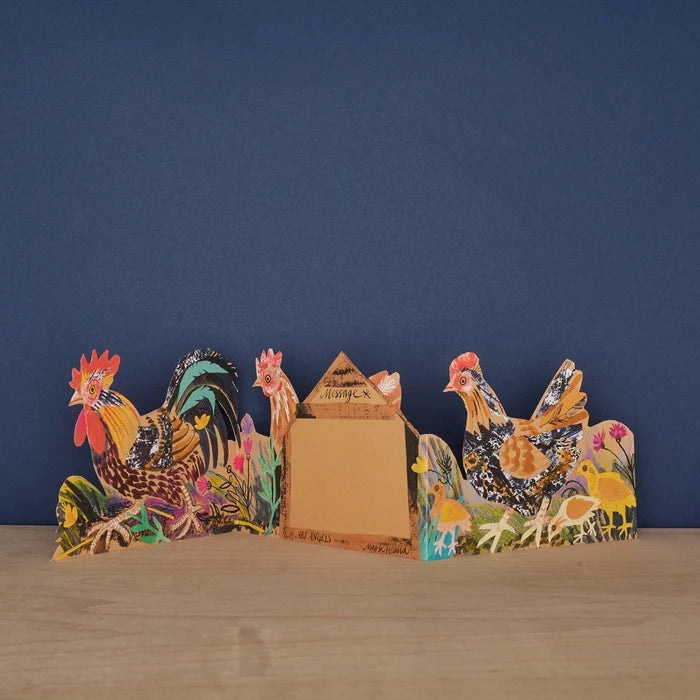 Three panels of a card with a rooster with a floral background shown unfolded on a wooden surface against a navy wall, shown from the back with middle panel displaying a 'message' text box