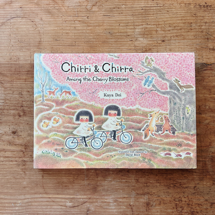 Book titled 'Chitri & Chirra Among the Cherry Blossoms' by Kaya Doi on a wooden surface