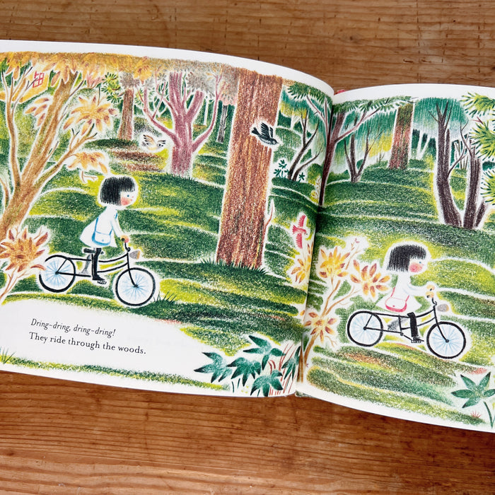 Illustrated book open to a page with a child on a bicycle in a forest setting.