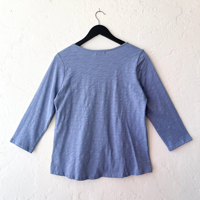 Blue long-sleeve shirt on a hanger against a white wall
