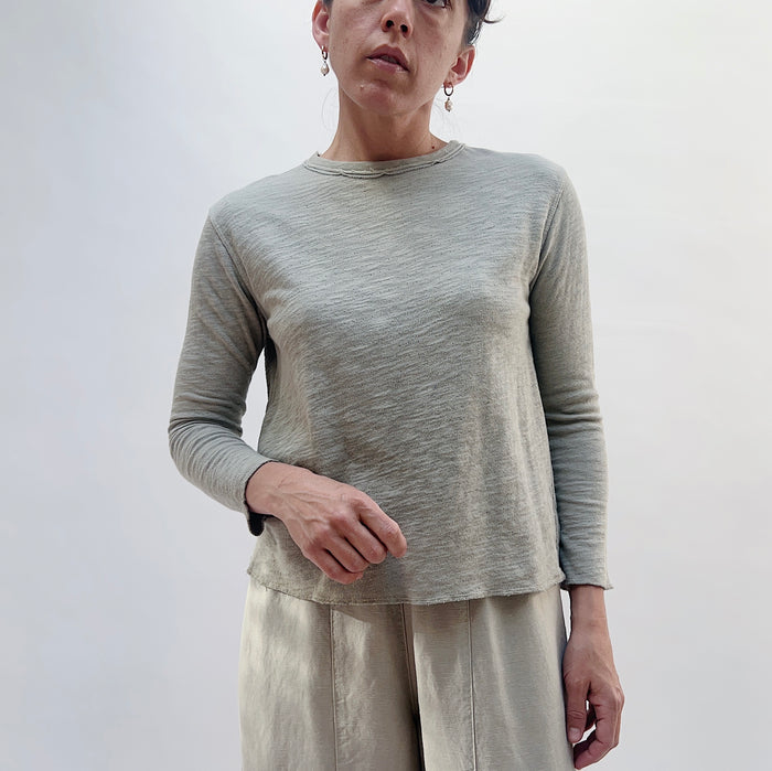 Front view of model wearing North Star Base artichoke crop double cotton tee, showing raw-edge crew neckline, relaxed boxy fit, and curved raw hem at hip
