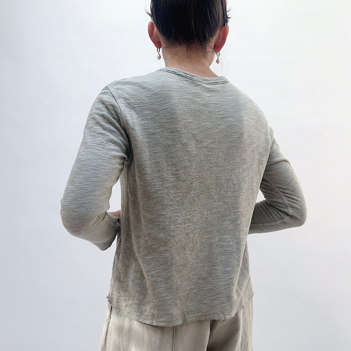 Back view of model wearing North Star Base artichoke crop double cotton tee, showing double-layered texture, long sleeves, and curved raw hem