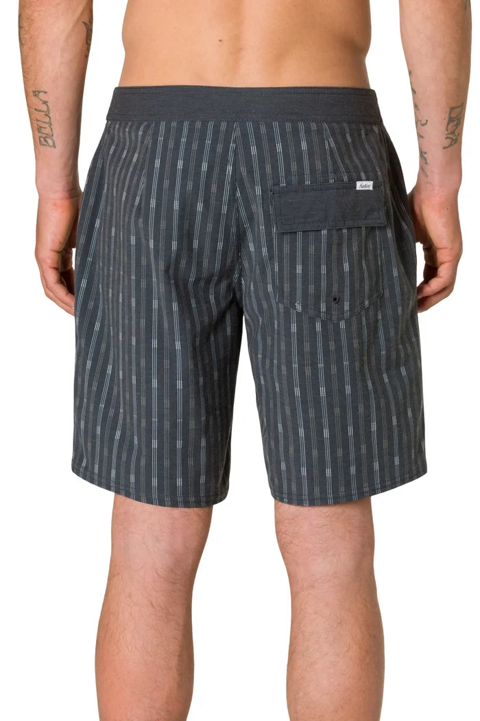 Rear view of a tattooed man wearing the Katin Crossroads Hybrid Trunk in Black Wash, showing the vertical stripe print, back patch pocket with velcro closure, and woven Katin label on the waistband