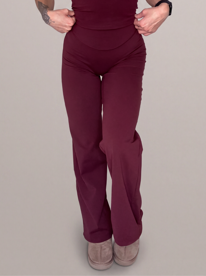 A model wearing a matching wine two-piece set consisting of a spaghetti-strap camisole top and high-waisted wide-leg pants, shown against a solid light gray background.