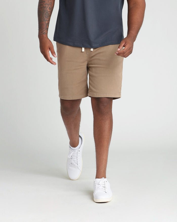 Man wearing dark khaki athletic fit shorts with drawstring waist and white sneakers.
