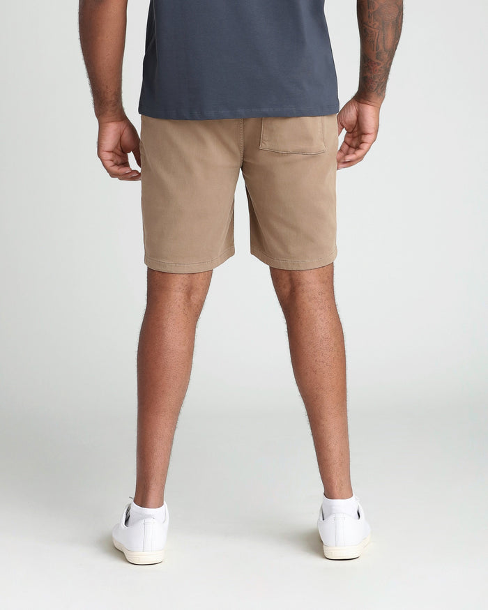 Tan athletic fit shorts with back pocket, worn with navy shirt and white sneakers.