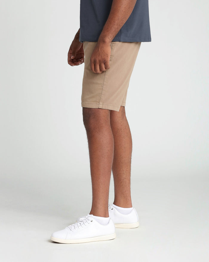 Man wearing dark khaki athletic fit shorts with a navy shirt and white sneakers.
