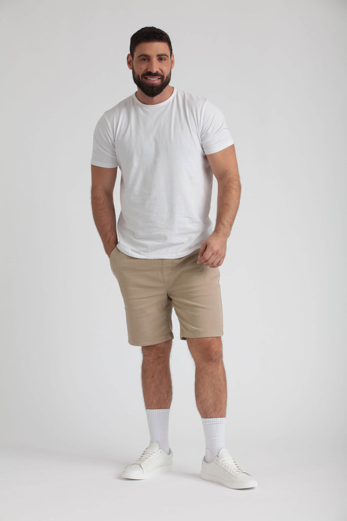 Man wearing light khaki athletic fit shorts with white t-shirt, white socks, and white sneakers.