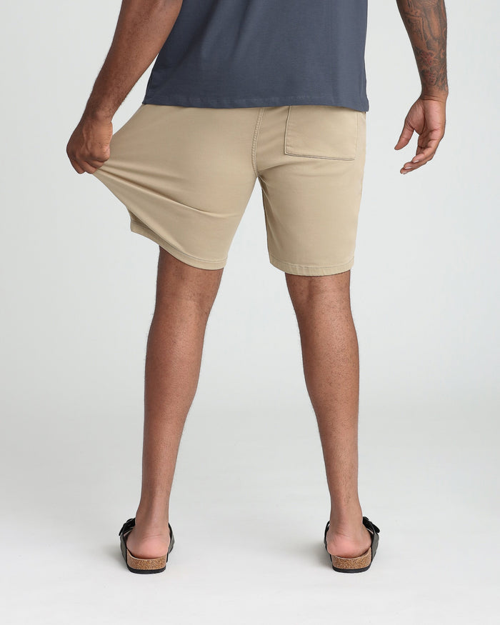 Man wearing light khaki athletic fit shorts with back pocket detail, paired with dark navy shirt.