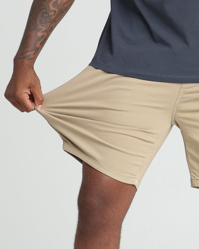 Light khaki athletic fit shorts shown on model with navy shirt, displaying side pocket and relaxed fit.