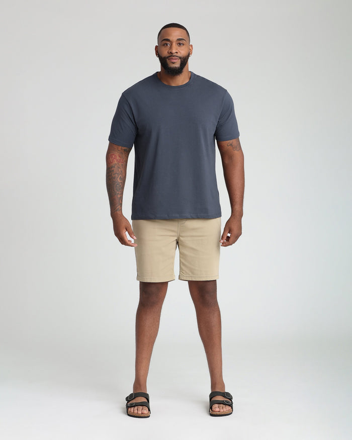 Man wearing light khaki athletic fit shorts with a dark blue t-shirt and black sandals.