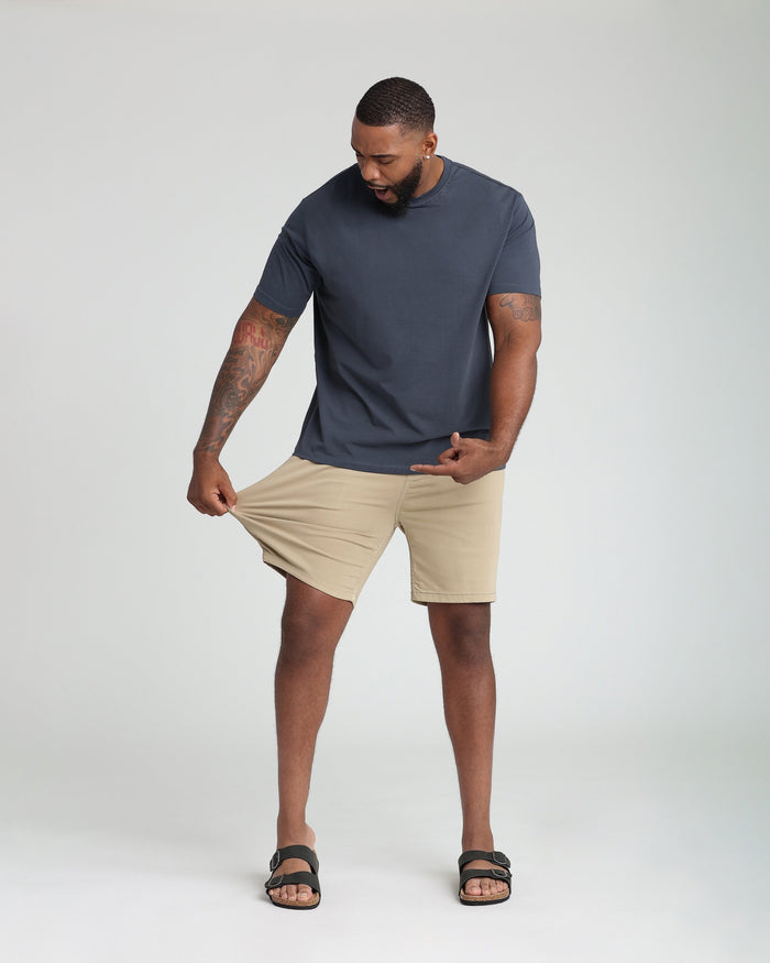 Man wearing light khaki athletic fit shorts with navy t-shirt and black sandals.