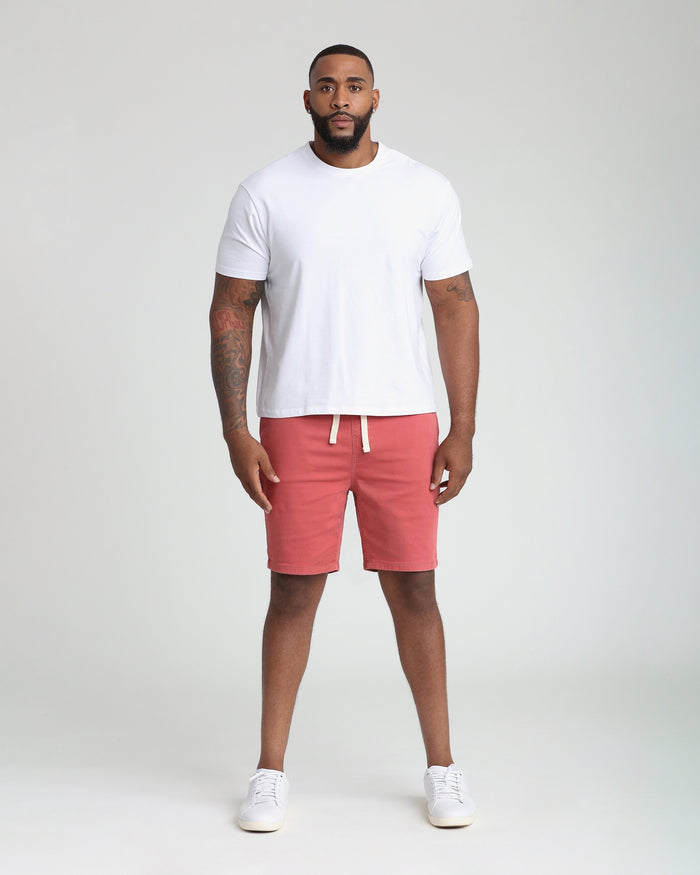 Man wearing white t-shirt and nantucket red athletic shorts with drawstring waist and white sneakers.