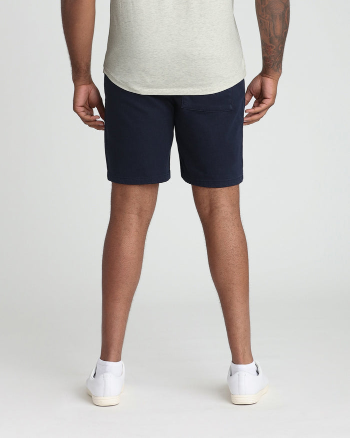 Man wearing navy athletic shorts with gray t-shirt and white socks, back view.