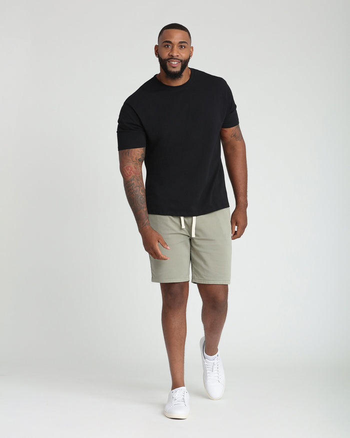 Man wearing light green athletic fit shorts with drawstring waist and black short-sleeve t-shirt.