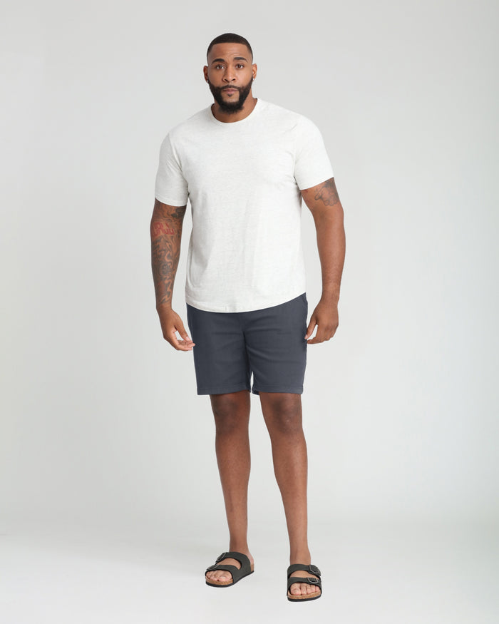 Man wearing white t-shirt and slate athletic shorts with black slide sandals.
