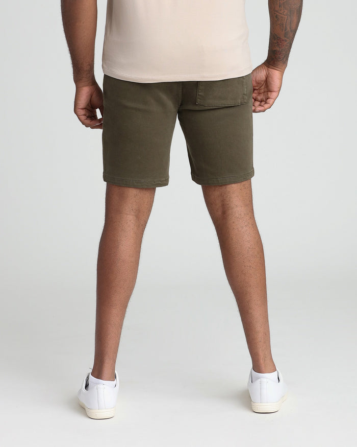 Man wearing soldier olive athletic shorts with cream t-shirt and white sneakers, shown from behind.